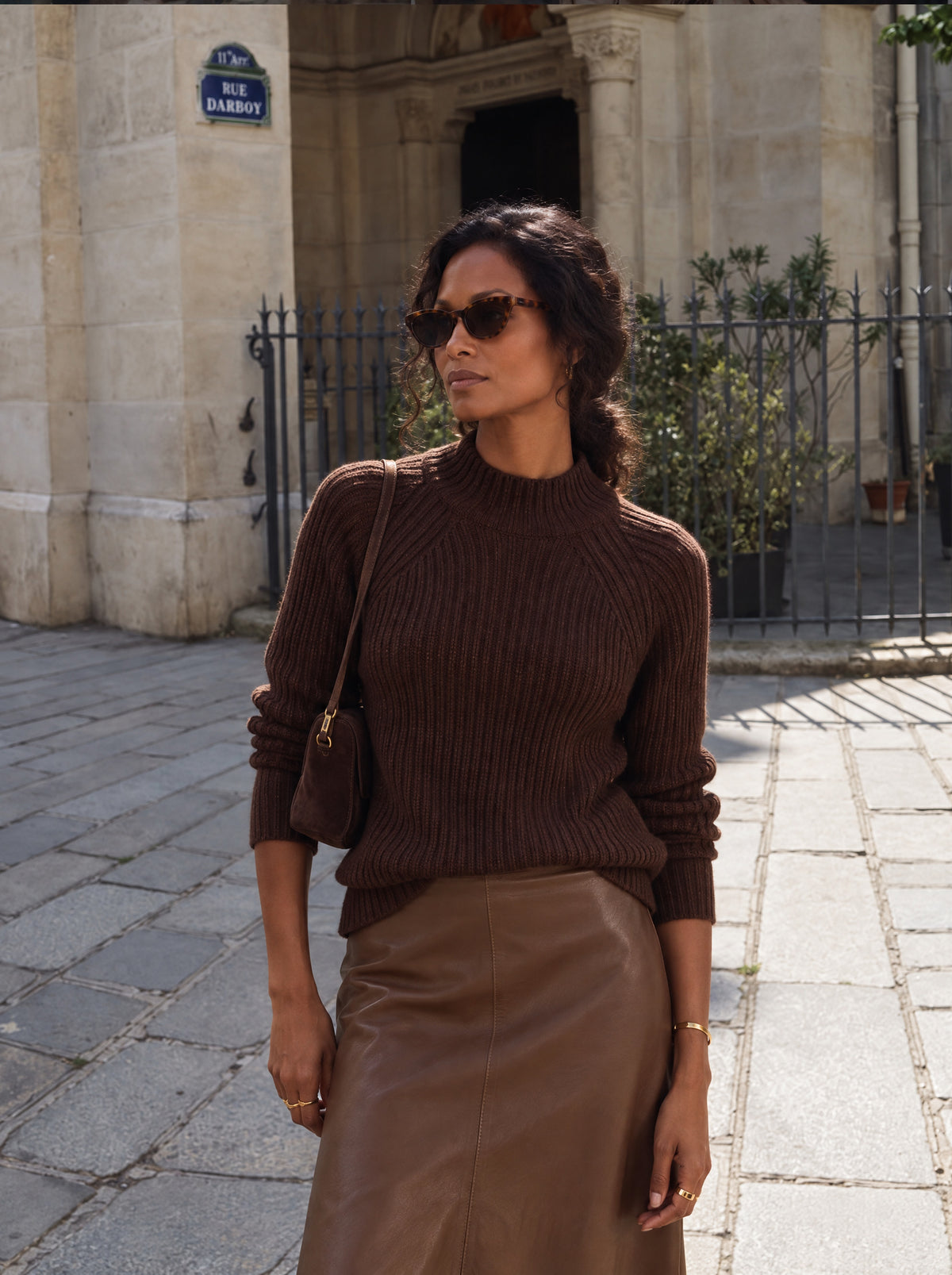 Vrouw draagt de Lize Pullover in bruin, een grof geribde trui met opstaande kraag, op de Sky Skirt in cognac van vegan leather